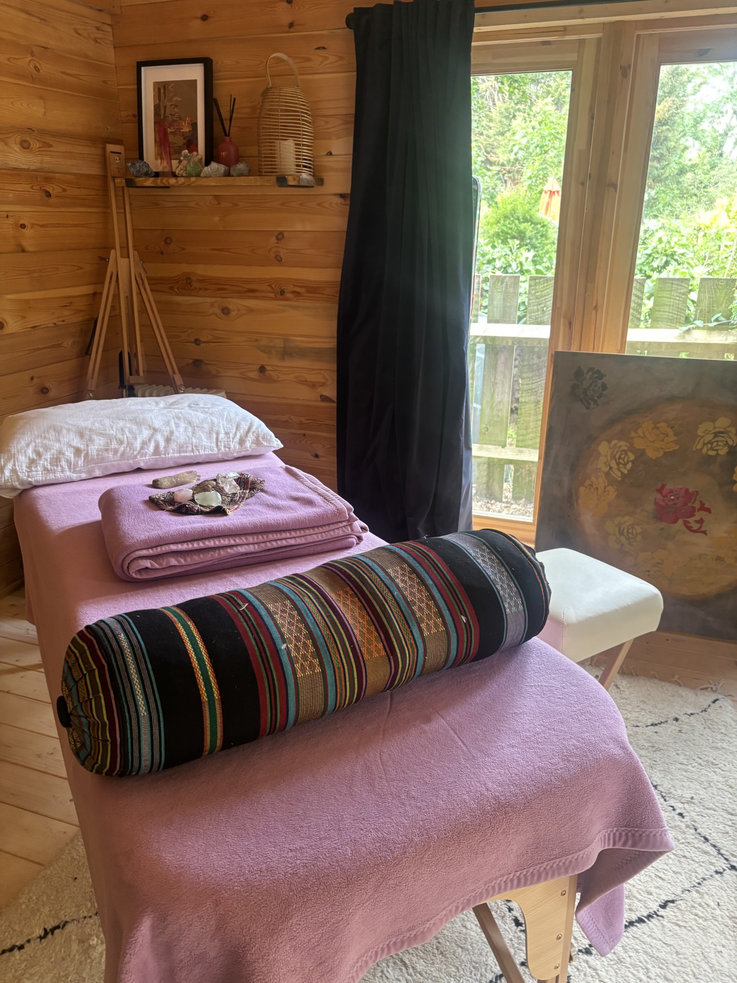 Cosy wood-panelled Reiki treatment room with crystals and a treatment table overlooking the garden